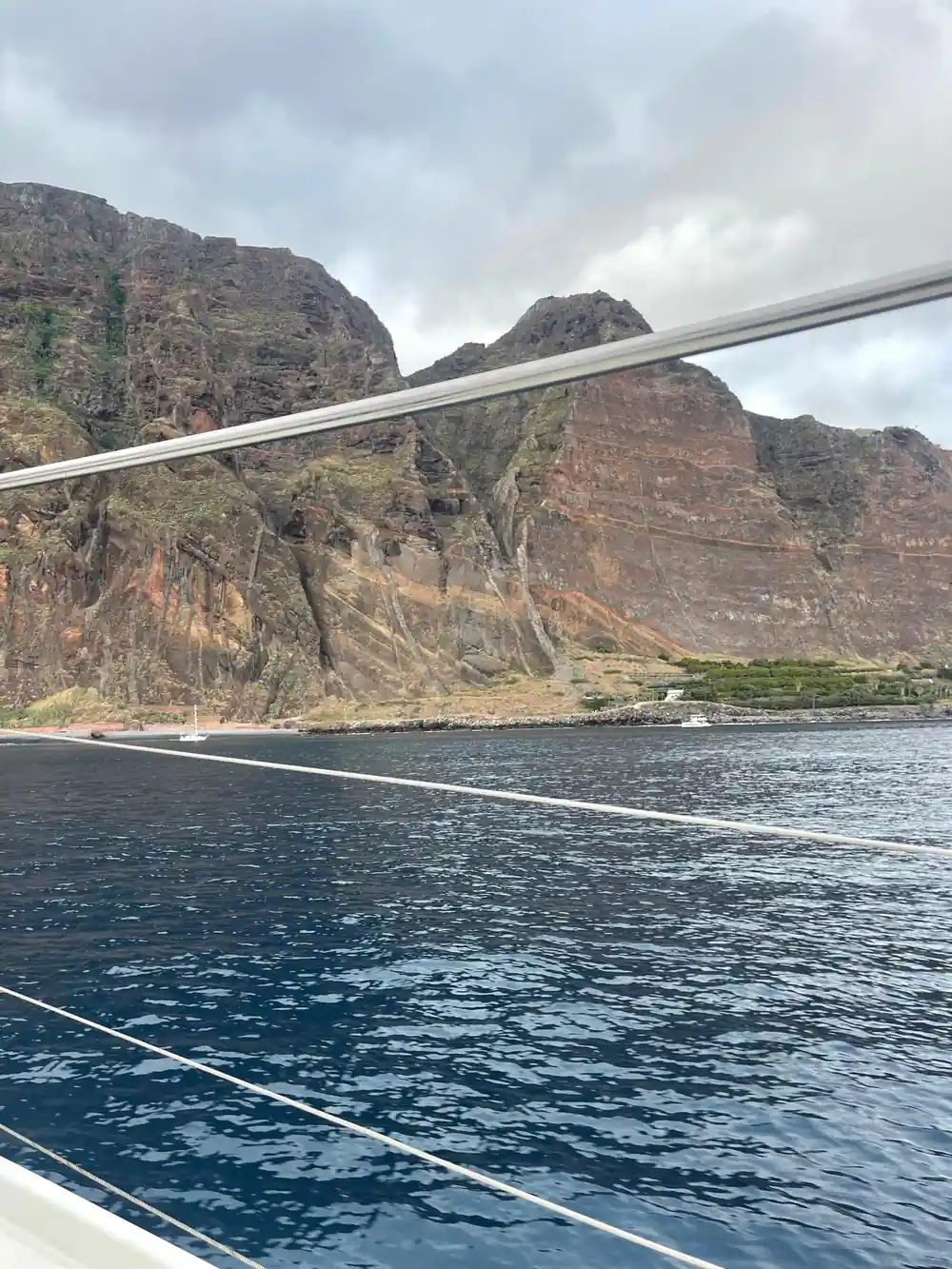 A big cliff and green slope seen past the boat's rigging