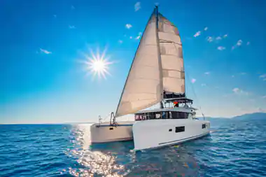 The catamaran under full sail on bright blue water with the sun overhead