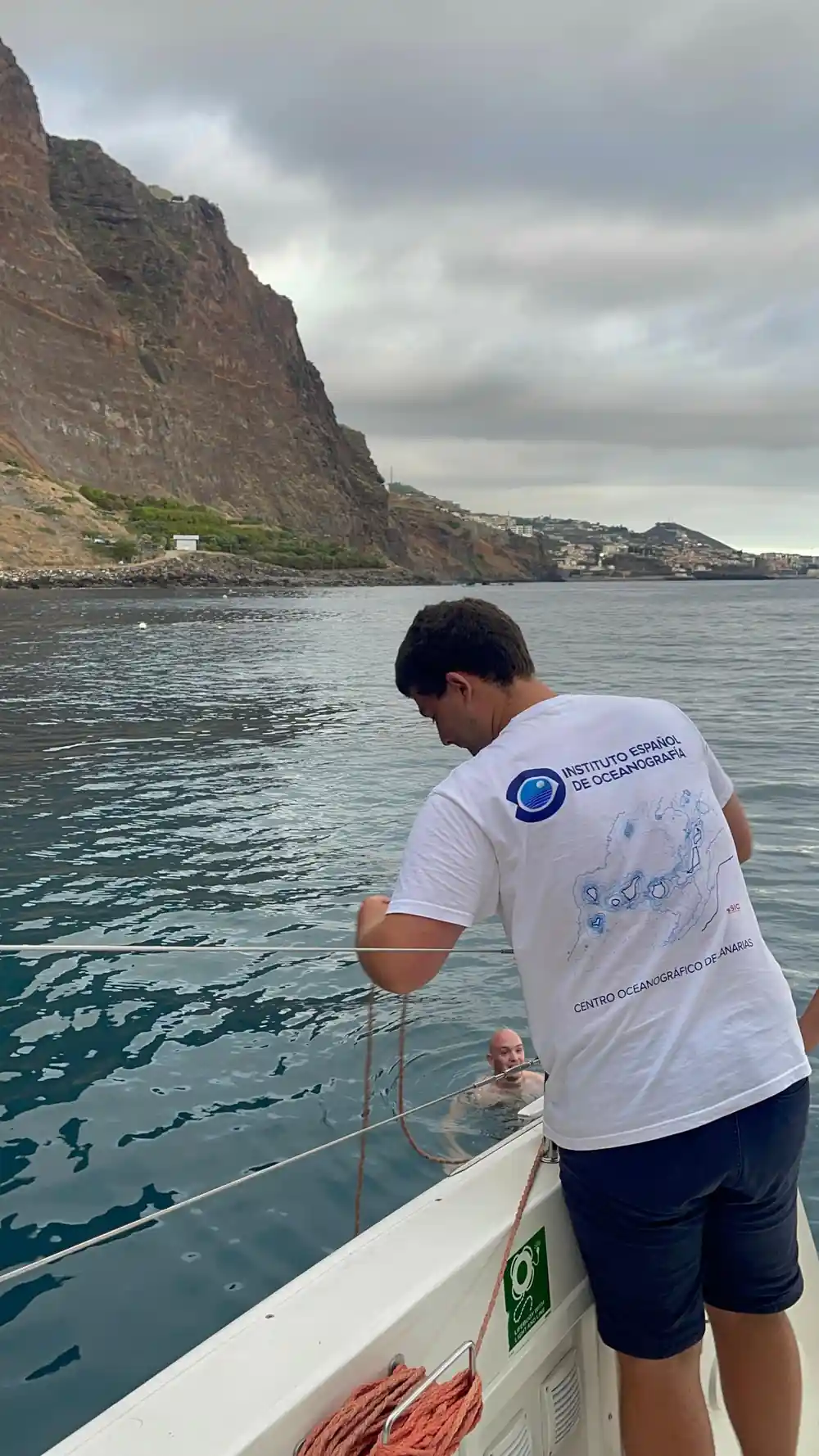 A crew member leaning over the side to look at the water