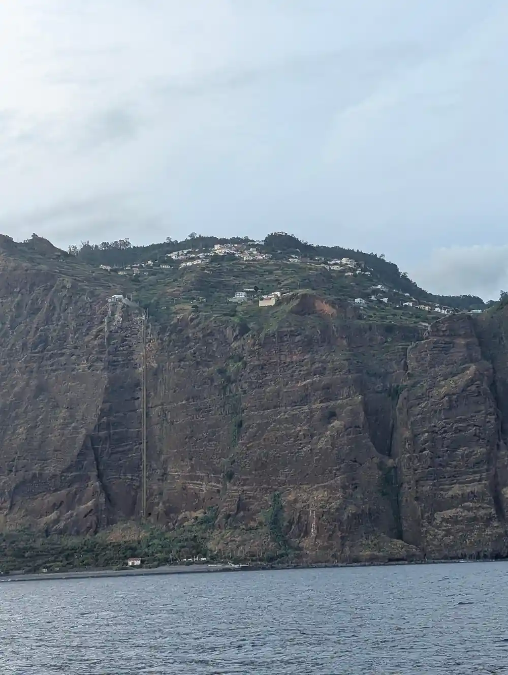 A high green cliff with houses on the ridge above the sea
