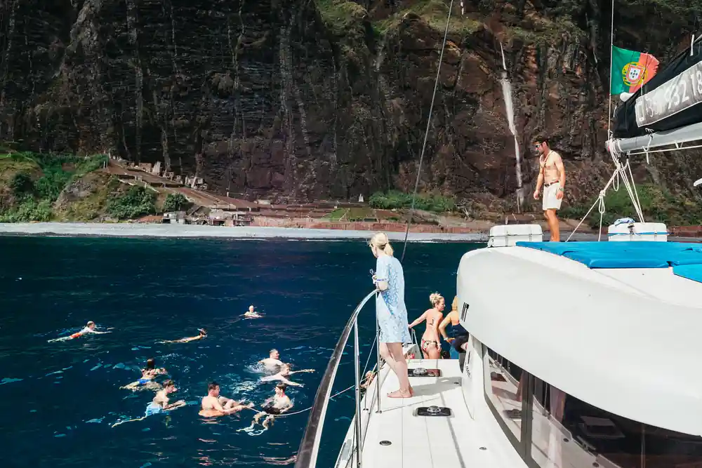 Swimmers in the water beside the catamaran below a green cliff